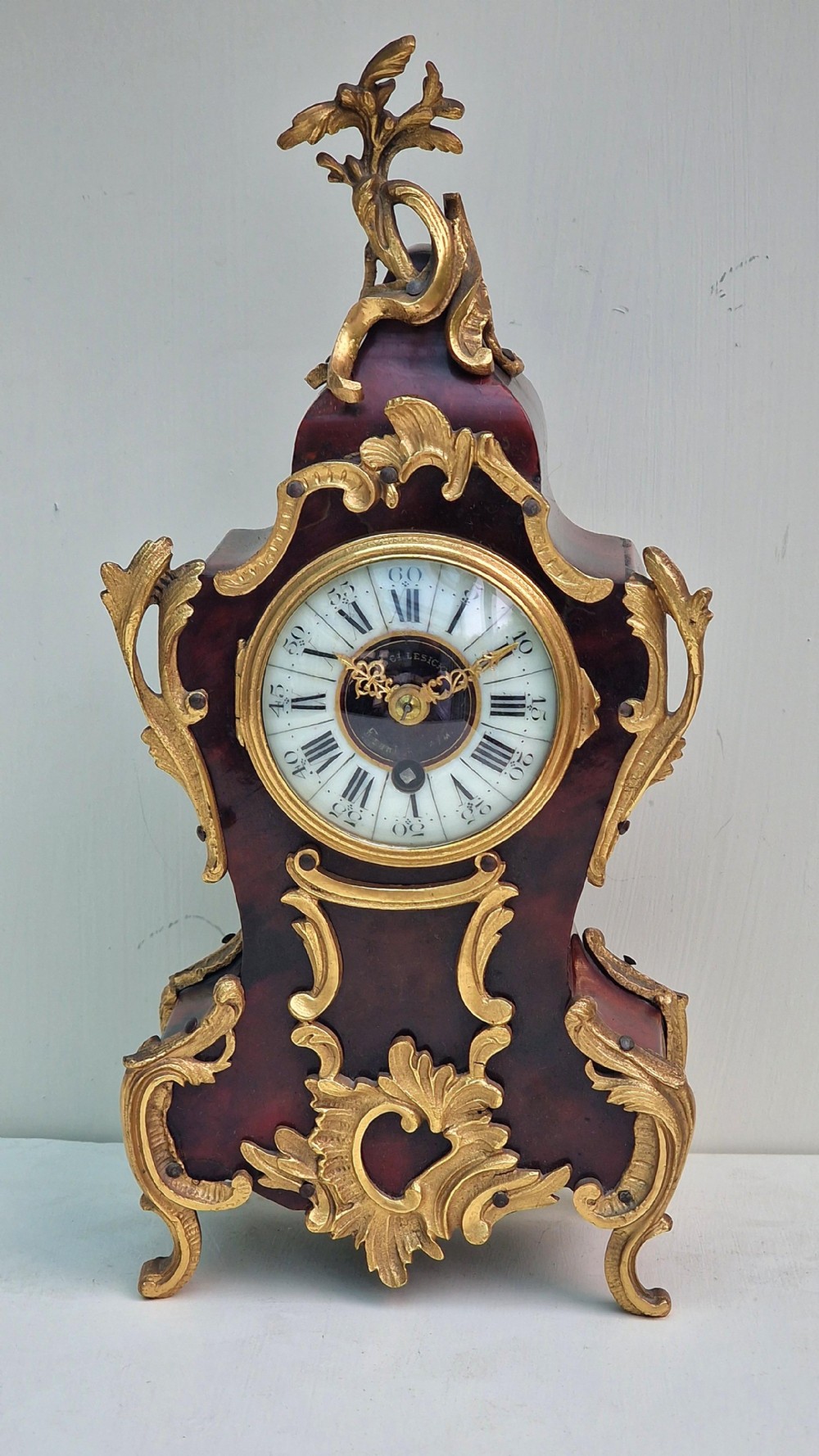 A miniature Louis XV style mantel clock featuring a dark red tortoiseshell case adorned with ornate gilt bronze Rococo mounts and a white enamel dial.