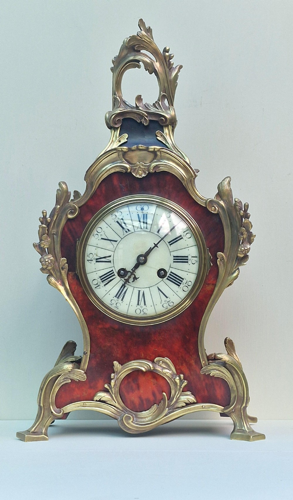 A French Louis XV style tortoiseshell and ormolu mantel clock featuring a curved frame, foliage mounts, and a white enamel dial with Roman numerals.