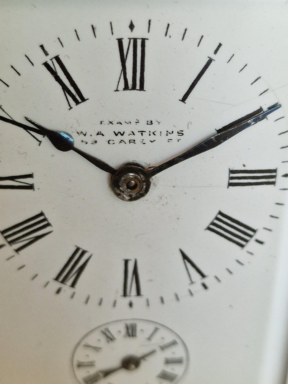A rectangular brass carriage clock featuring bevelled glass side panels, a hinged top carrying handle, and a white enamel dial with Roman numerals. View II