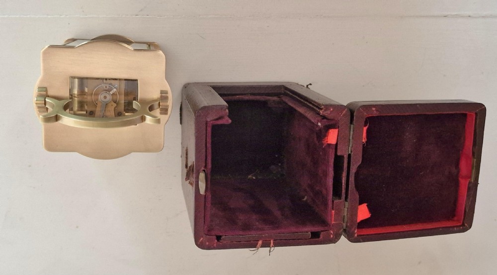 A brass serpentine carriage clock featuring a white enamel dial with Roman numerals, bevelled glass panels, and an arched carrying handle. View IV