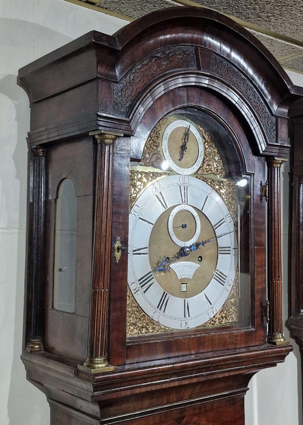 A Georgian flame mahogany longcase clock featuring a brass dial with silvered chapter ring and carved arched hood. View V