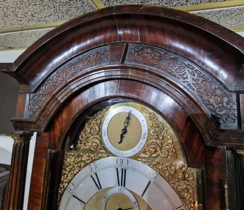 A Georgian flame mahogany longcase clock featuring a brass dial with silvered chapter ring and carved arched hood. View VII