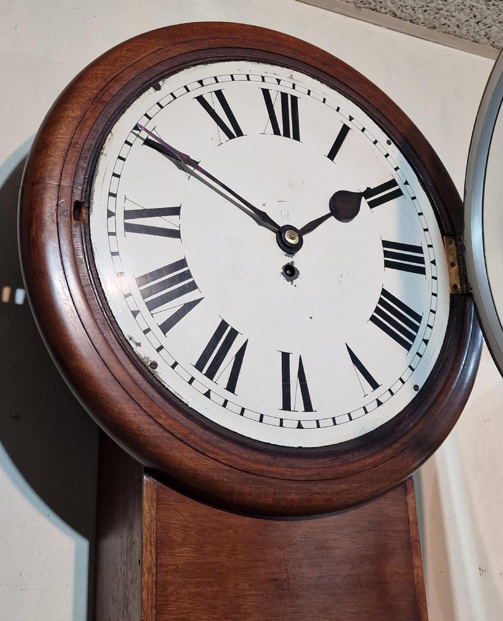 An antique George V mahogany drop dial wall clock featuring a circular painted dial with black Roman numerals and a brass bezel. View III