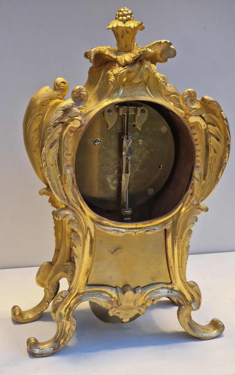 An ornate gilt metal mantel clock featuring rococo scrollwork, an acanthus leaf finial, and a circular engine-turned dial with Roman numerals. View II