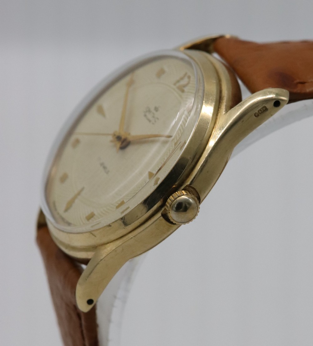 A vintage mid-century Smiths De Luxe wristwatch featuring a 9ct gold round case, textured cream dial with gold hour markers, and a tan leather strap. View III