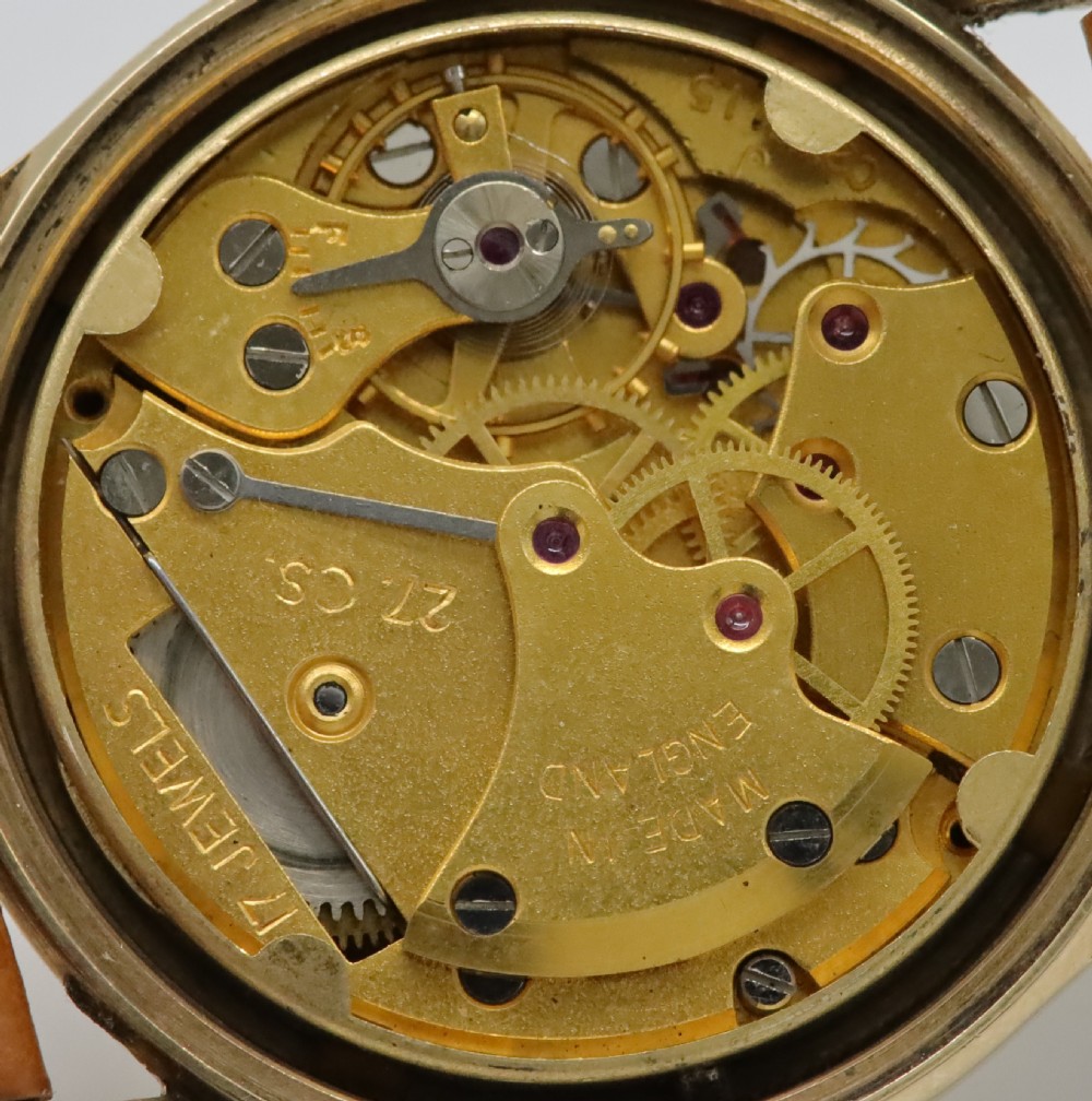 A vintage mid-century Smiths De Luxe wristwatch featuring a 9ct gold round case, textured cream dial with gold hour markers, and a tan leather strap. View VII