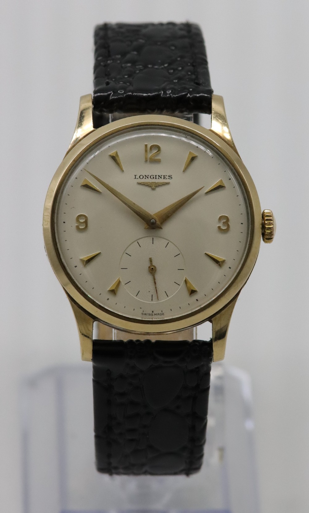A vintage 1962 Longines wristwatch featuring a circular 9K gold case, cream dial with gold hour markers, sub-seconds dial, and a black leather strap.