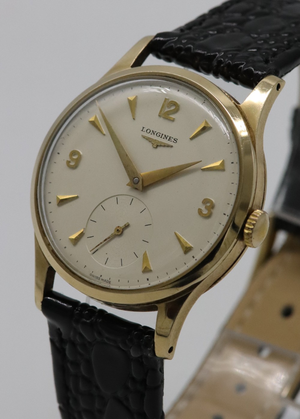 A vintage 1962 Longines wristwatch featuring a circular 9K gold case, cream dial with gold hour markers, sub-seconds dial, and a black leather strap. View II