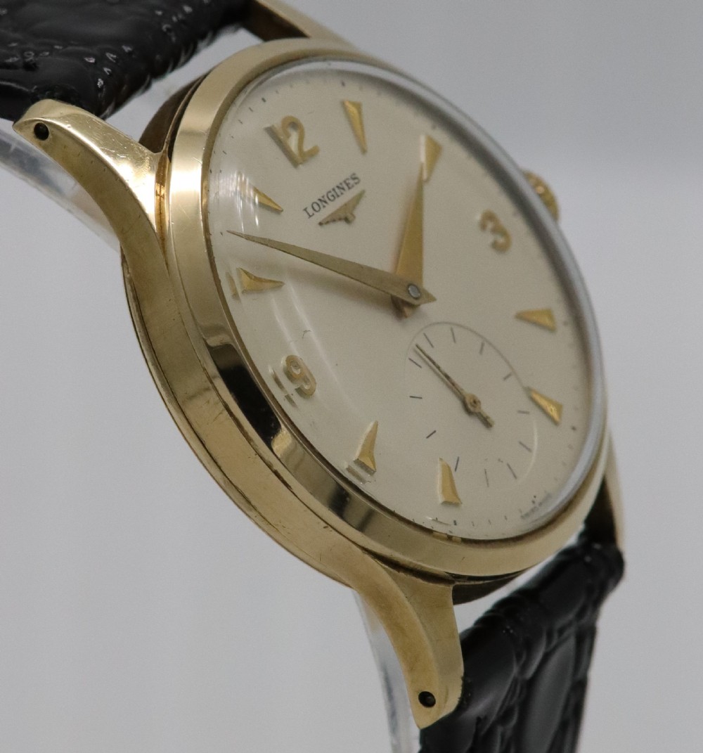 A vintage 1962 Longines wristwatch featuring a circular 9K gold case, cream dial with gold hour markers, sub-seconds dial, and a black leather strap. View VI