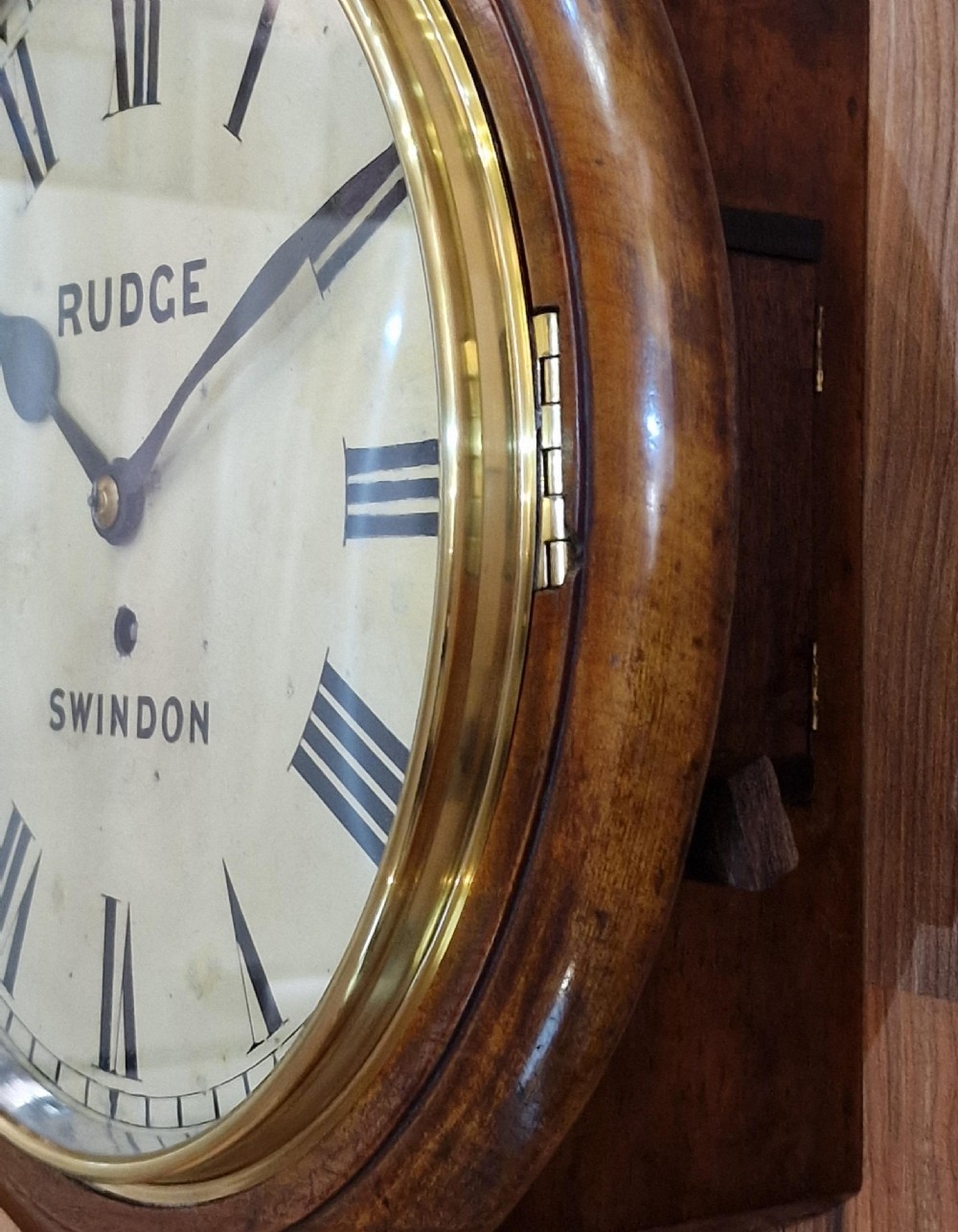 A circular Victorian mahogany fusee dial wall clock featuring a white face with Roman numerals, a brass bezel, and black spade hands, marked Rudge Swindon. View IV
