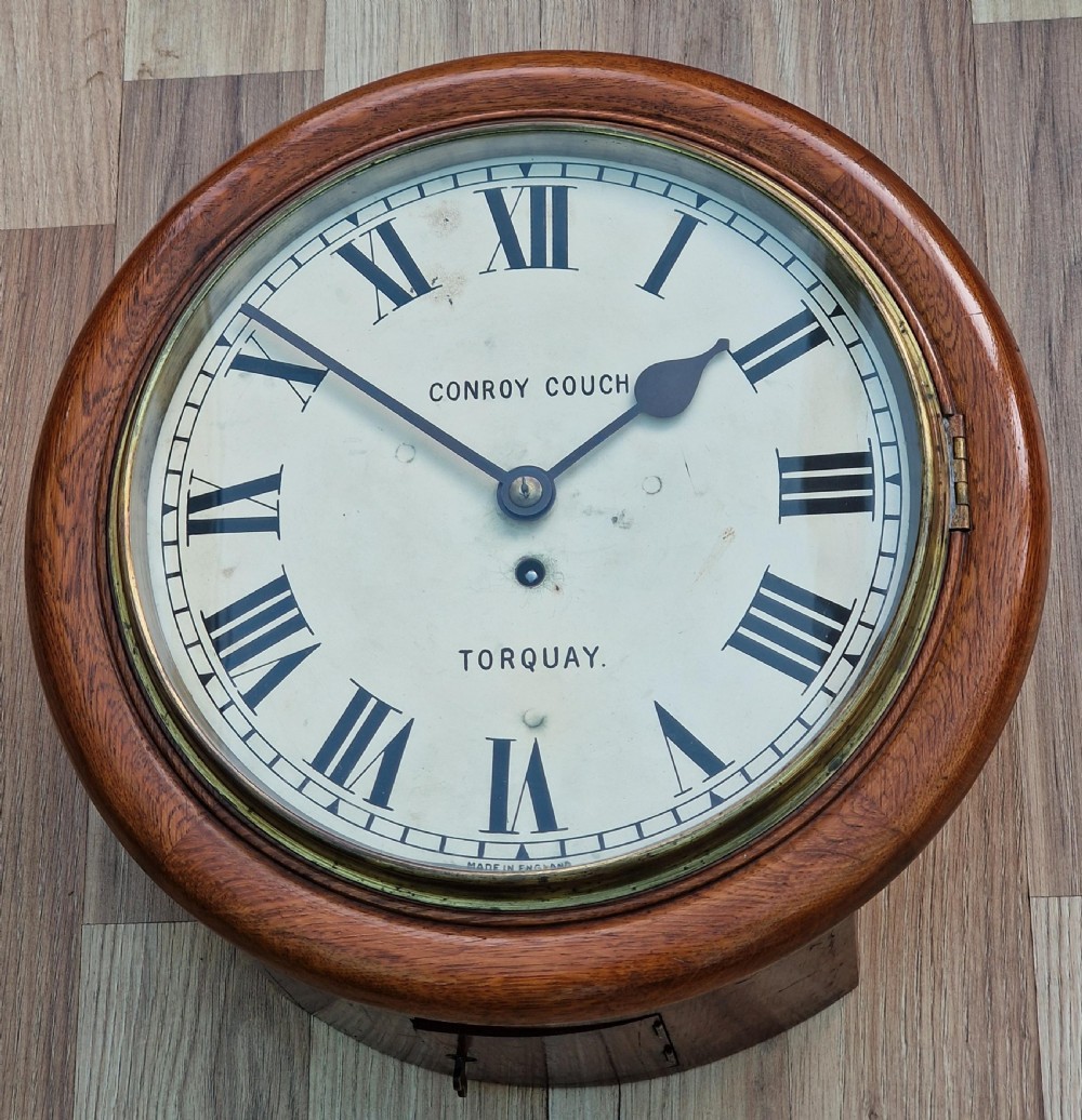 A circular mahogany wall clock with a white painted dial featuring black Roman numerals and black metal hands behind a glass bezel.