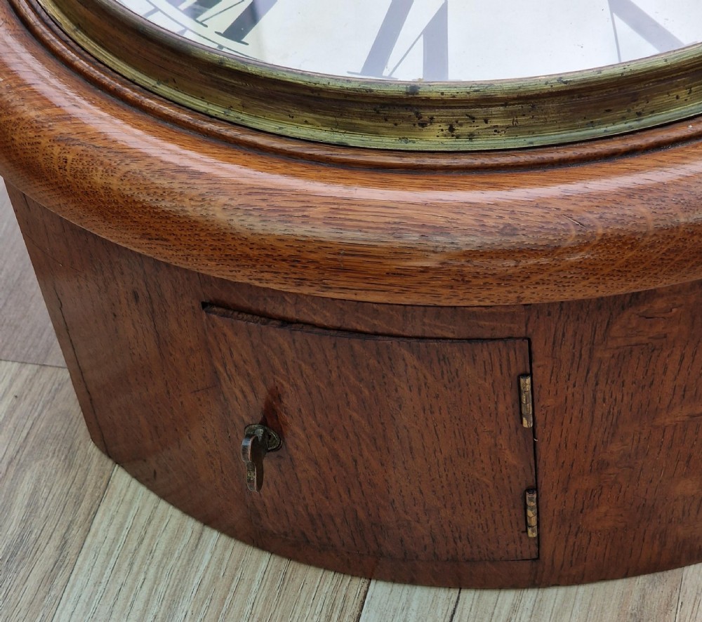 A circular mahogany wall clock with a white painted dial featuring black Roman numerals and black metal hands behind a glass bezel. View II