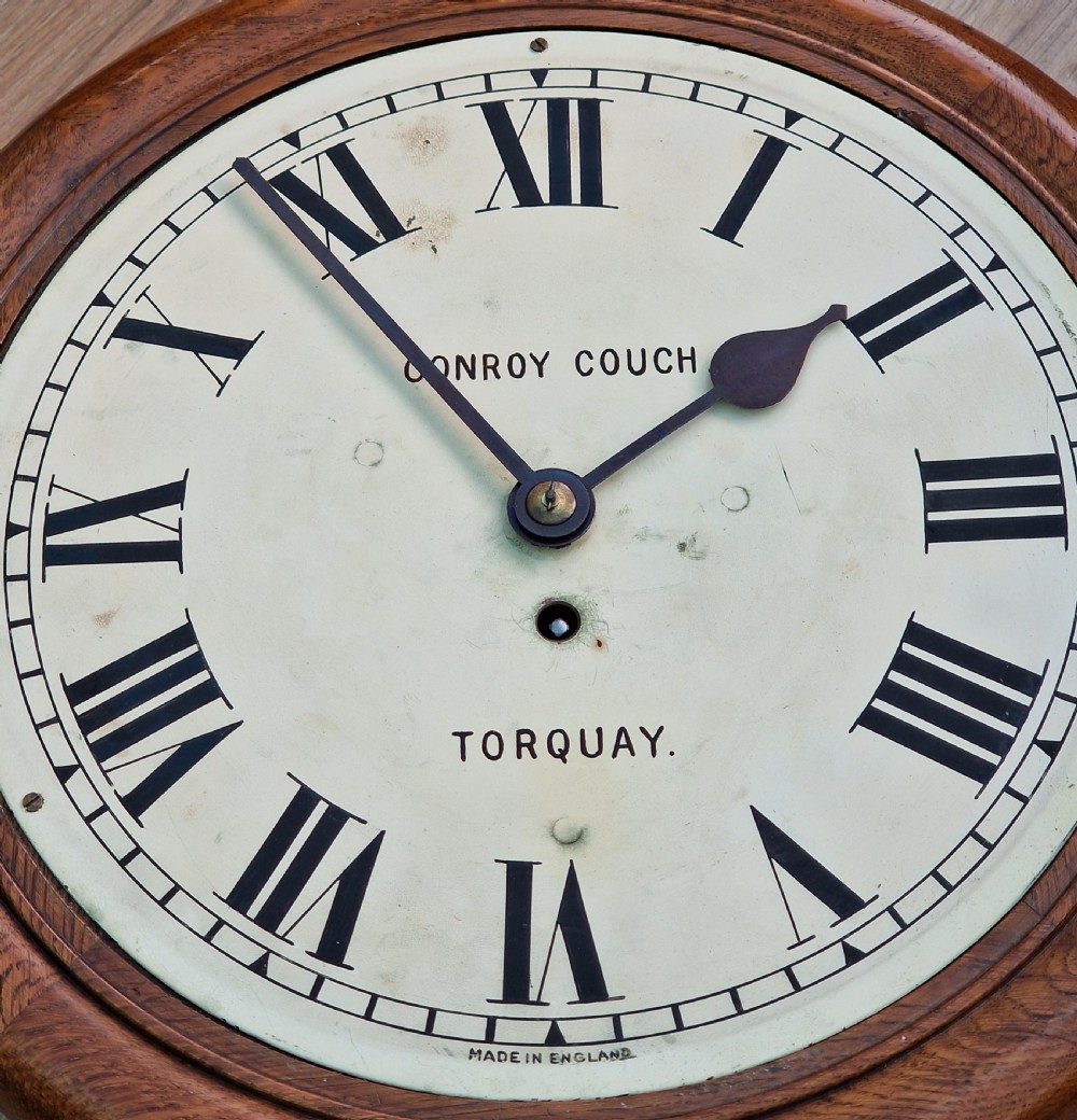 A circular mahogany wall clock with a white painted dial featuring black Roman numerals and black metal hands behind a glass bezel. View IV