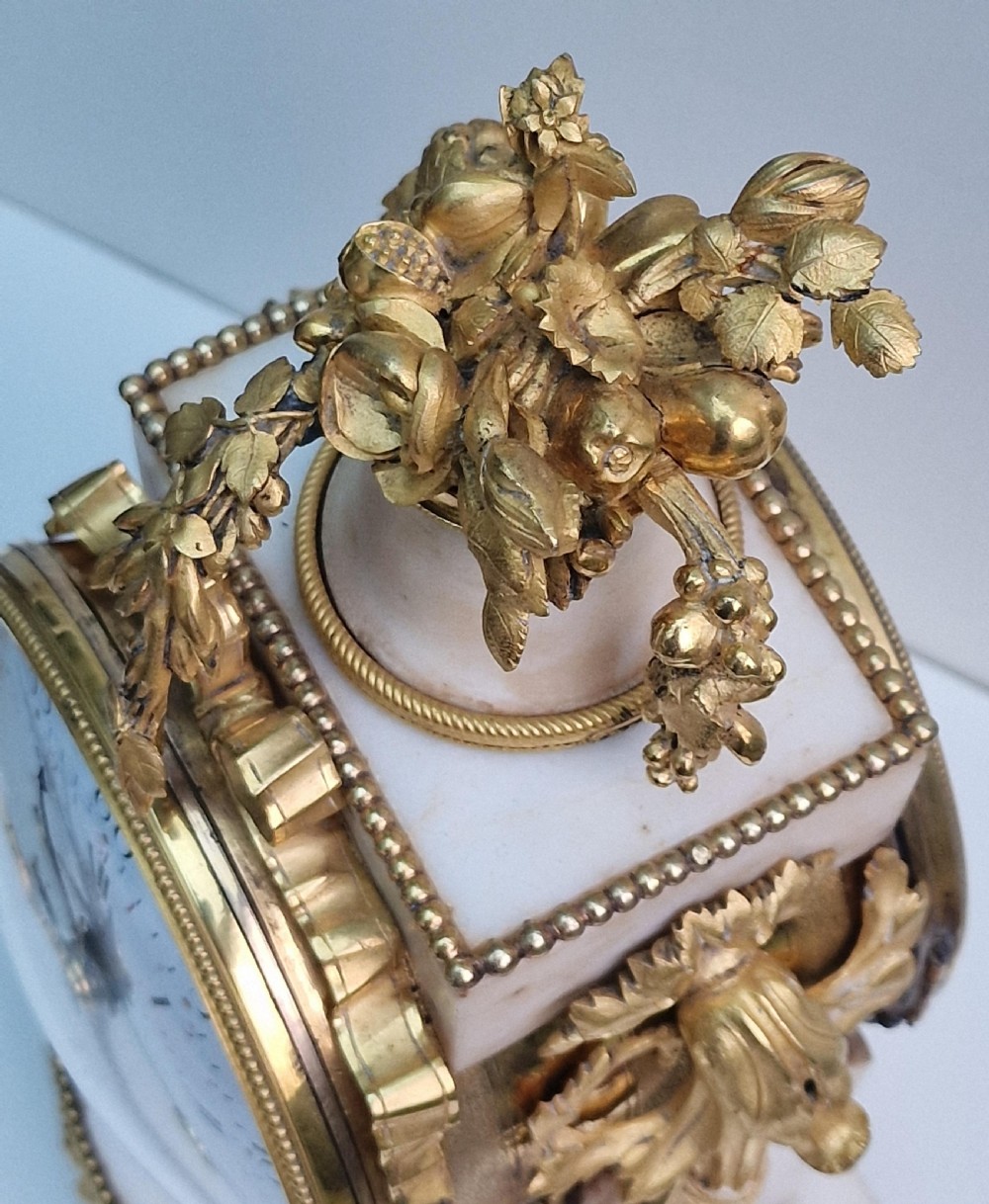 An antique Louis XVI style white marble and gilt bronze mantel clock featuring a calendar enamel dial and floral garland mounts. View VIII