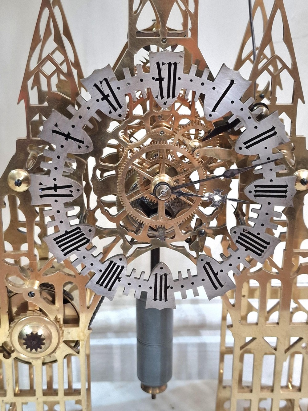 A Victorian Gothic revival brass skeleton clock featuring pierced cathedral spires, a silvered Roman numeral dial, and a top bell, housed under a clear glass dome on a white marble plinth. View III