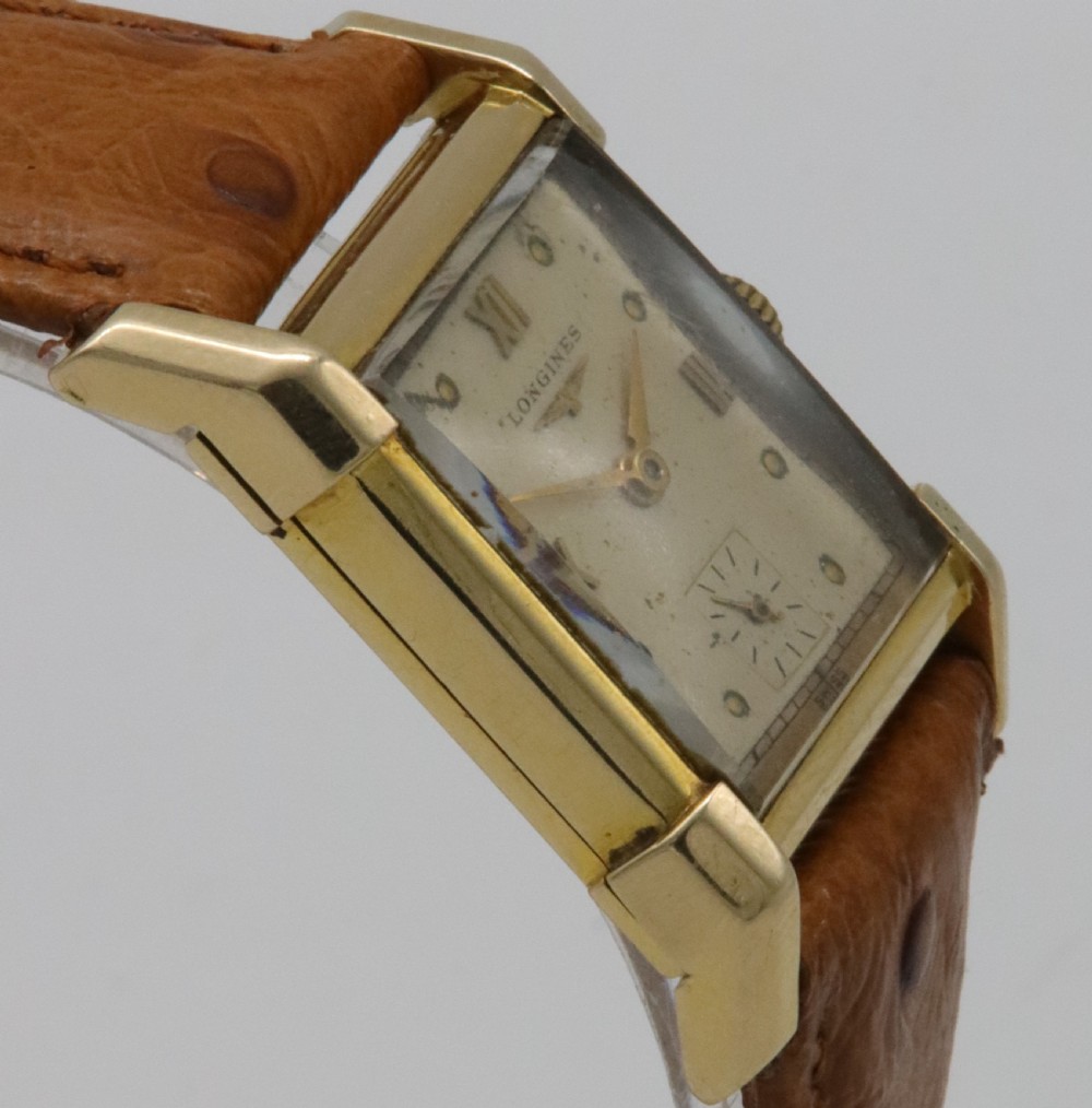 A 1949 Longines rectangular 14k gold wristwatch featuring a cream dial with sub-seconds register and a tan leather strap. View IV