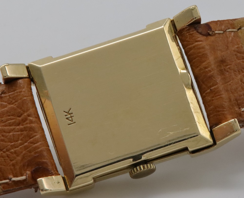 A 1949 Longines rectangular 14k gold wristwatch featuring a cream dial with sub-seconds register and a tan leather strap. View VI