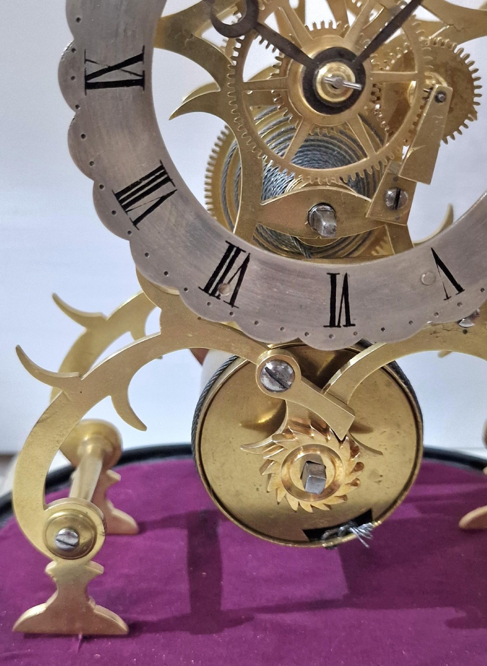A Victorian brass skeleton clock with an exposed movement and silvered chapter ring, displayed beneath a clear glass dome on an ebonised base. View III