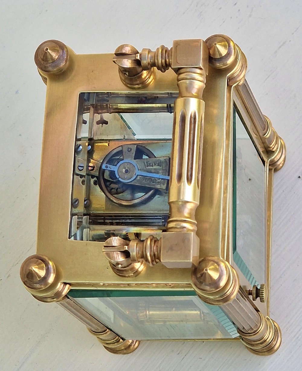 An antique brass carriage clock featuring bevelled glass panels, fluted corner columns, ornate foliage borders, and a white dial with Roman numerals. View IV