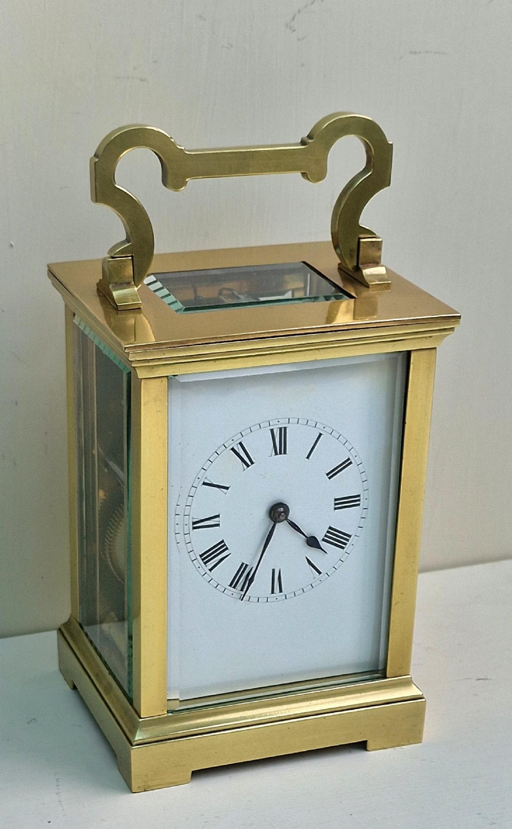 A rectangular French brass carriage clock with bevelled glass panels, a white enamel dial with black Roman numerals, and a shaped carrying handle.