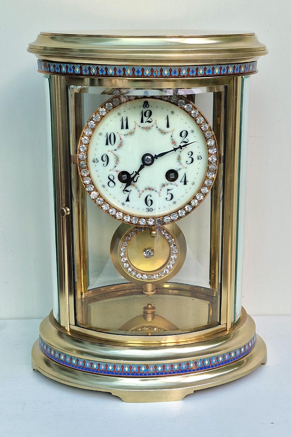 An antique oval brass four-glass mantel clock featuring enamel borders and a jewel-encrusted dial.