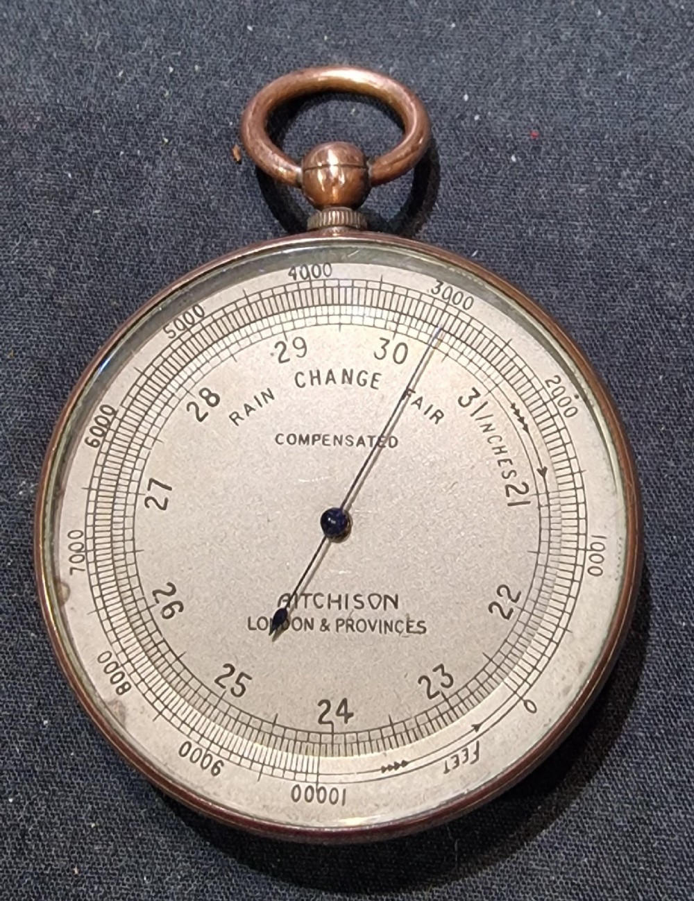 An antique pocket barometer by Aitchison London with a brass casing, silvered dial, and blued steel pointer.