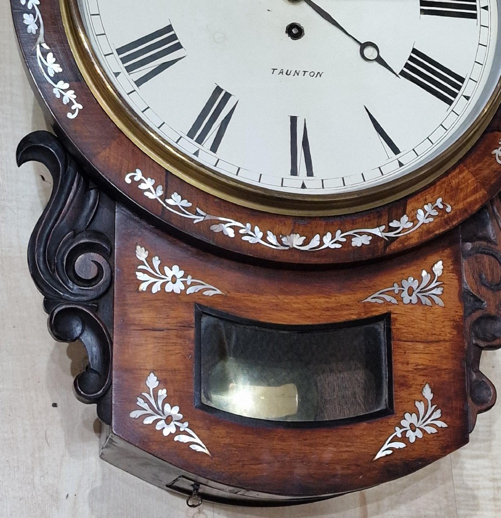 A Victorian mahogany drop dial wall clock featuring mother-of-pearl inlay, carved scroll sides, a brass bezel, and a white dial signed Chave Taunton with Roman numerals. View II