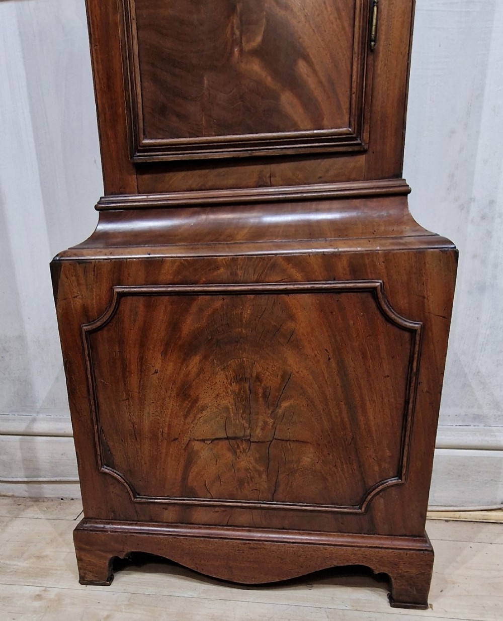 A tall Georgian flame mahogany longcase clock featuring an arched hood with brass finials, reeded columns, and a brass and silvered dial. View II