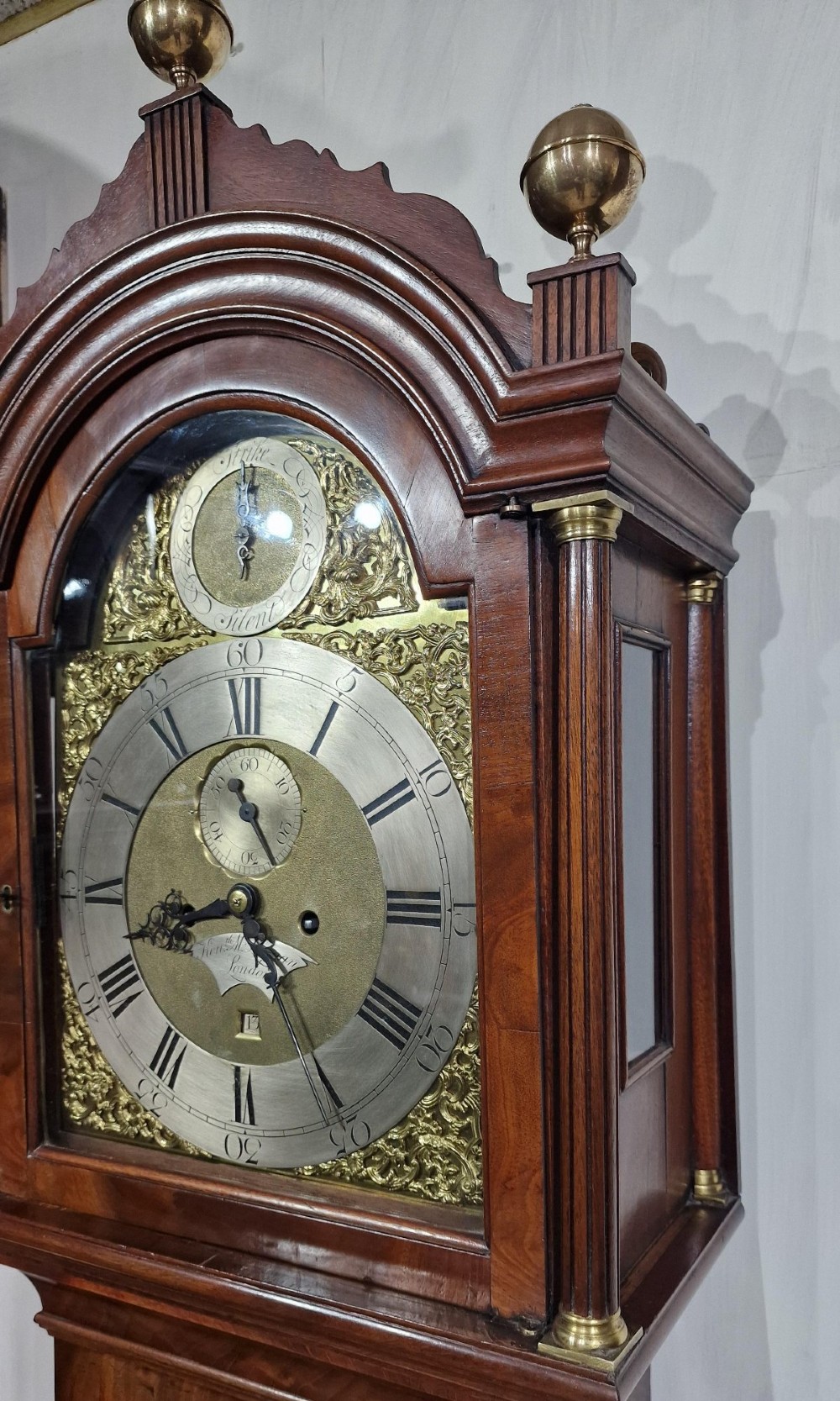 A tall Georgian flame mahogany longcase clock featuring an arched hood with brass finials, reeded columns, and a brass and silvered dial. View III
