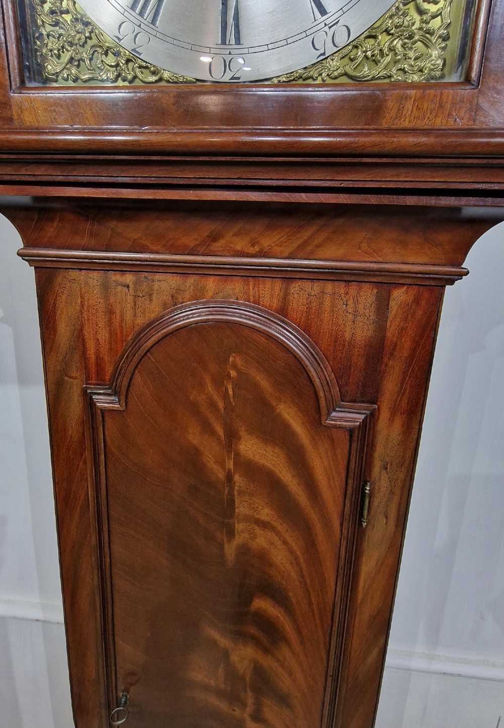 A tall Georgian flame mahogany longcase clock featuring an arched hood with brass finials, reeded columns, and a brass and silvered dial. View VI