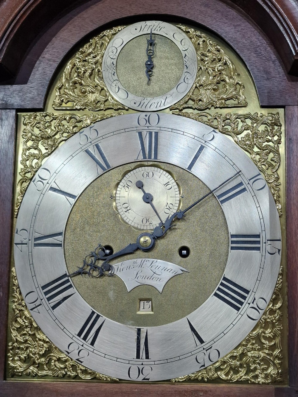 A tall Georgian flame mahogany longcase clock featuring an arched hood with brass finials, reeded columns, and a brass and silvered dial. View VIII