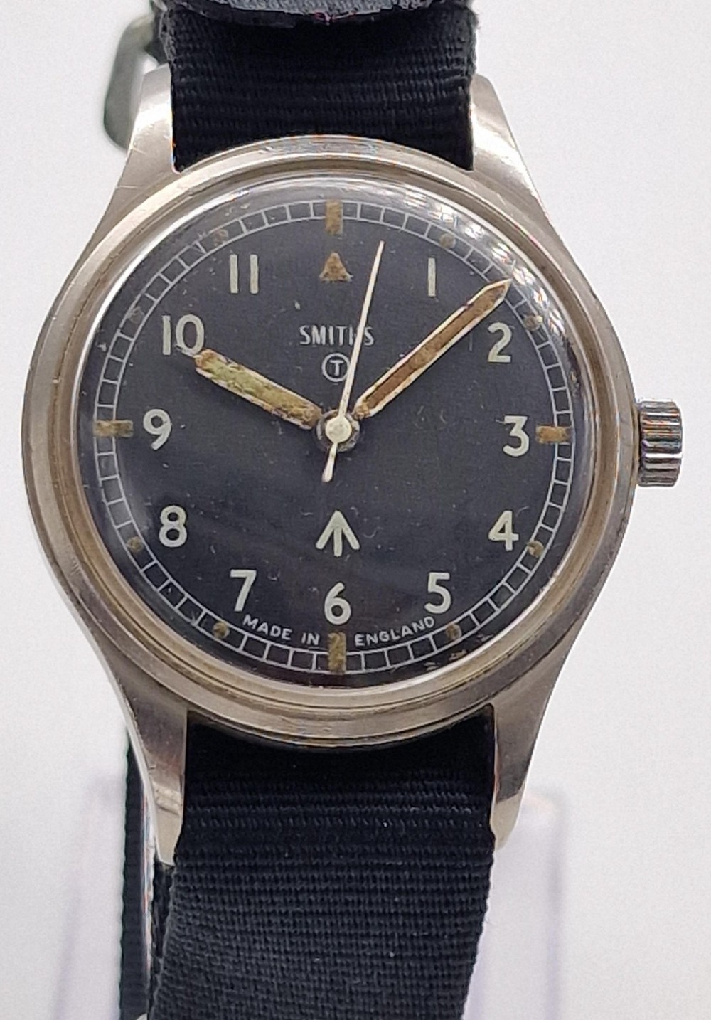 A Smiths W10 military wristwatch featuring a black dial with Arabic numerals, broad arrow mark, and a black strap.