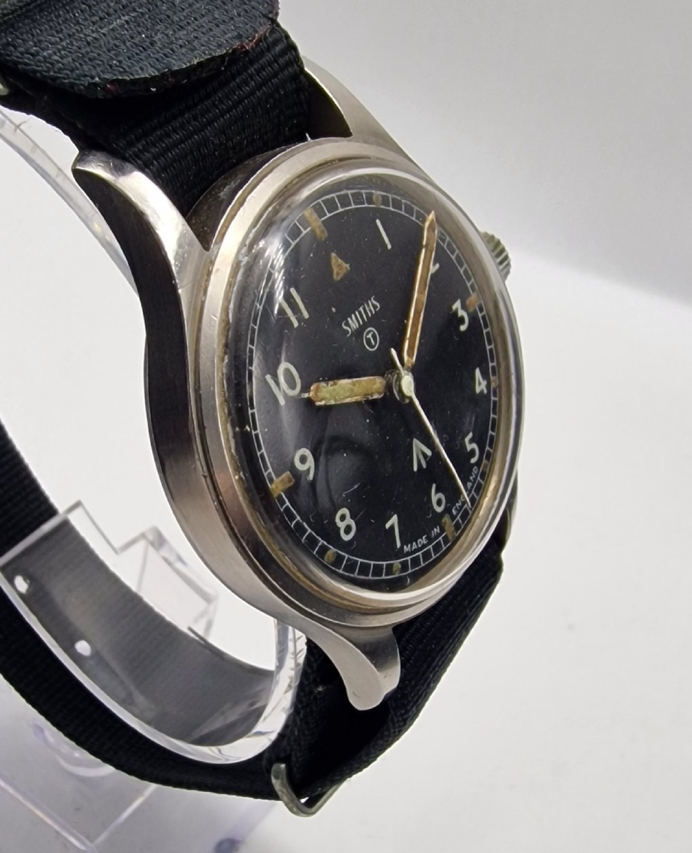 A Smiths W10 military wristwatch featuring a black dial with Arabic numerals, broad arrow mark, and a black strap. View II
