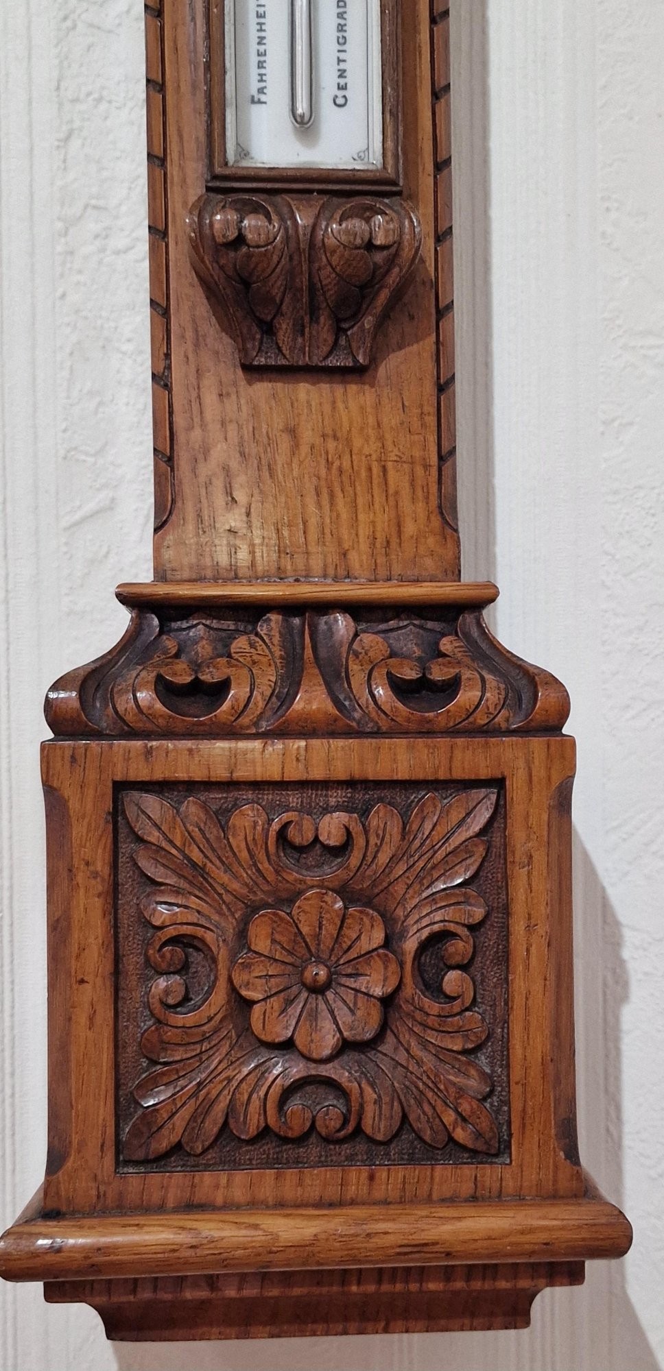 A carved Victorian oak stick barometer featuring an exposed mercury tube, dual weather scales, integrated thermometer, and a carved foliate cistern cover. View II