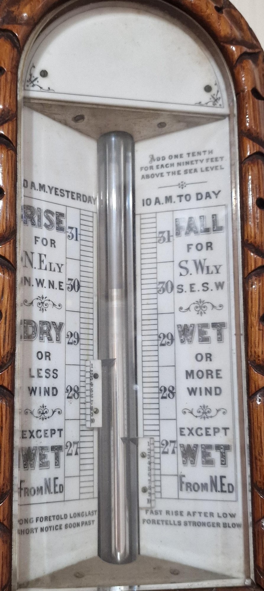 A carved Victorian oak stick barometer featuring an exposed mercury tube, dual weather scales, integrated thermometer, and a carved foliate cistern cover. View III