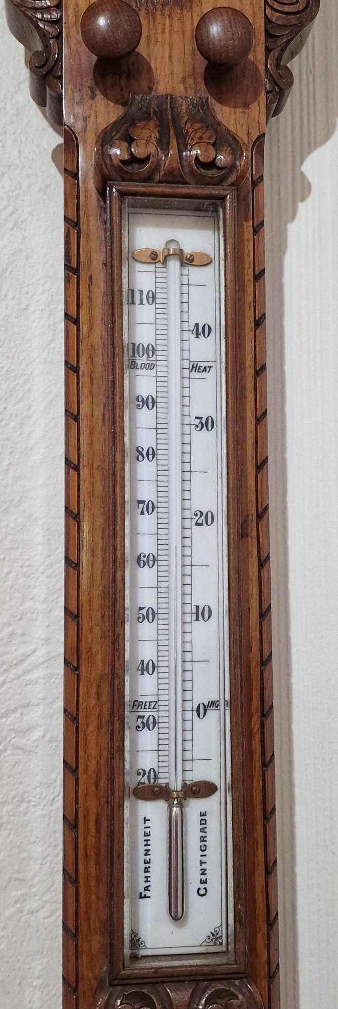 A carved Victorian oak stick barometer featuring an exposed mercury tube, dual weather scales, integrated thermometer, and a carved foliate cistern cover. View VI