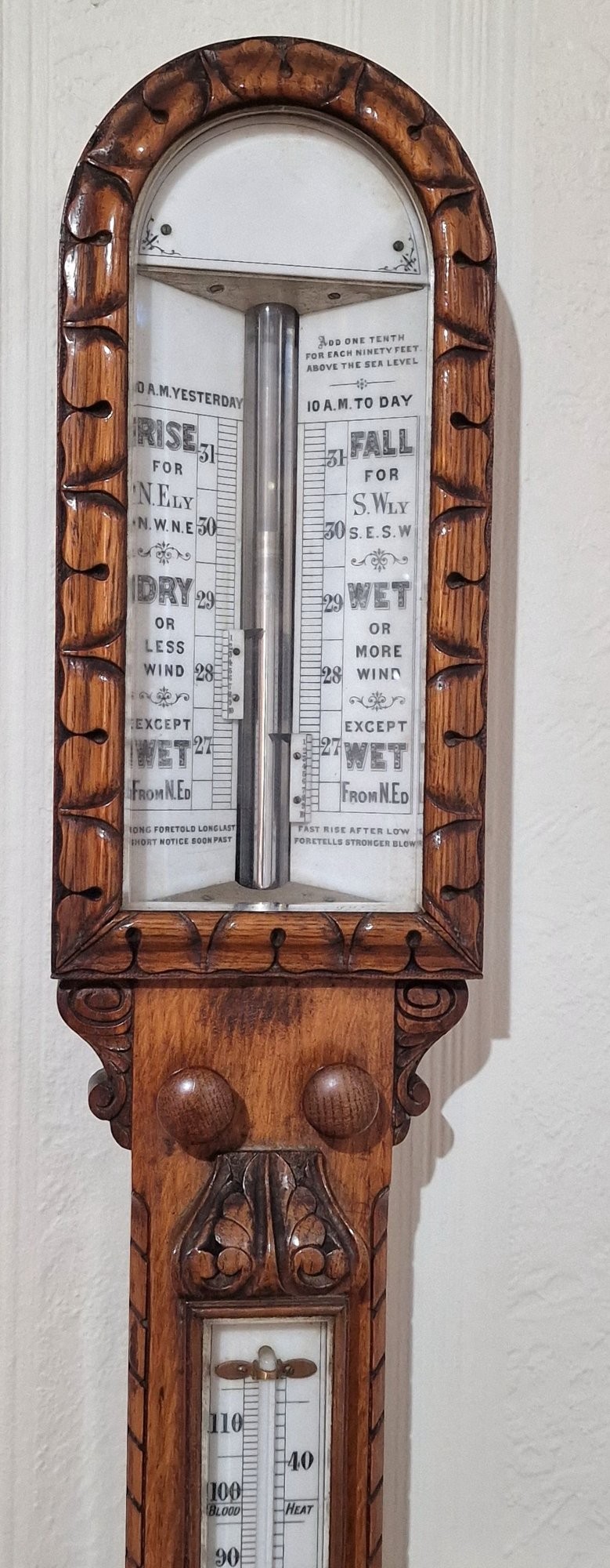 A carved Victorian oak stick barometer featuring an exposed mercury tube, dual weather scales, integrated thermometer, and a carved foliate cistern cover. View VII