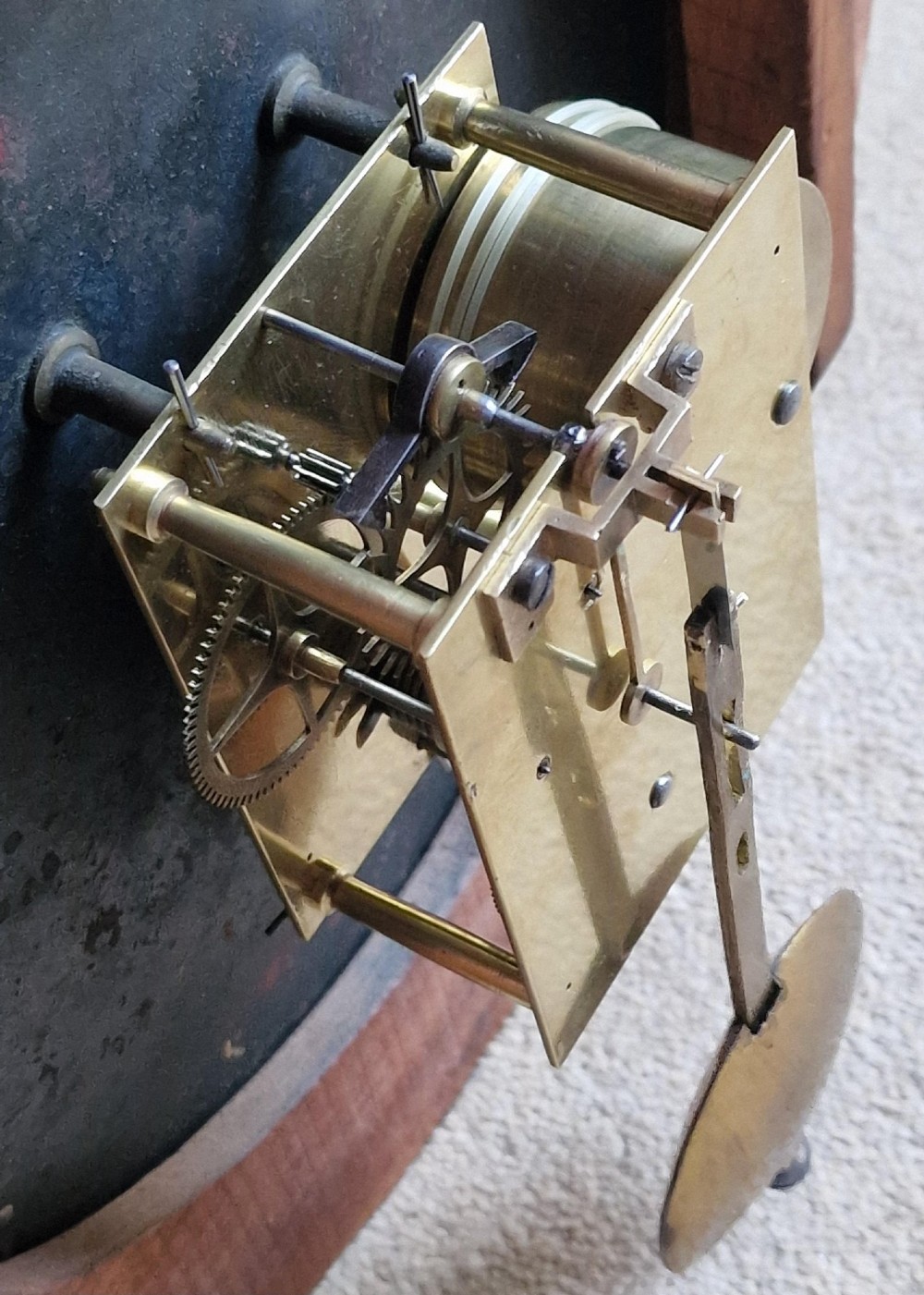 A circular antique mahogany wall clock featuring a cream dial with black Roman numerals and a hinged brass bezel. View III