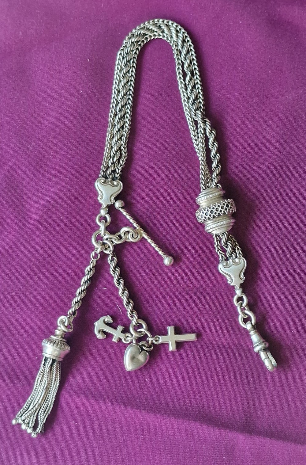 An antique silver chatelaine pocket watch chain featuring multi-strand braided rope links, a decorative slide barrel, a wire tassel, and suspended faith, hope, and charity charms.