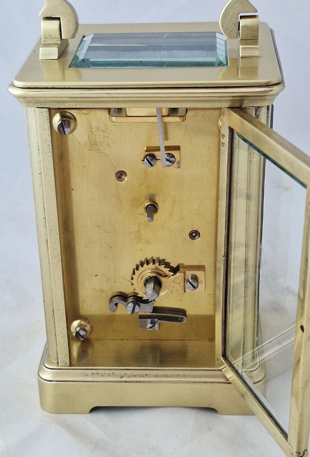 A rectangular brass carriage clock featuring a white enamel dial with Roman numerals, blued steel hands, bevelled glass panels, and a hinged carrying handle on top. View II
