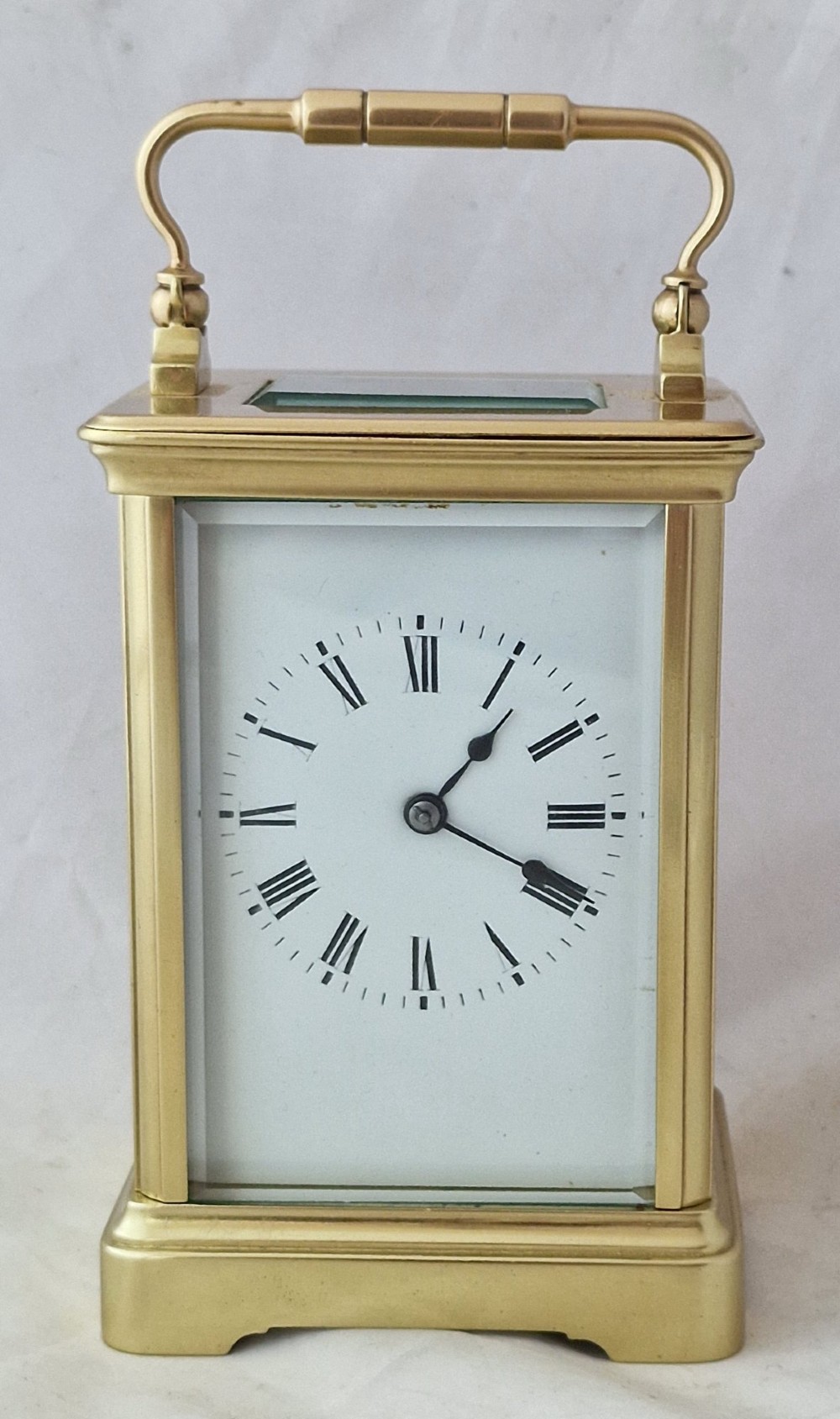 A brass carriage clock featuring bevelled glass side panels, a white enamel dial with black Roman numerals, and a top carrying handle.