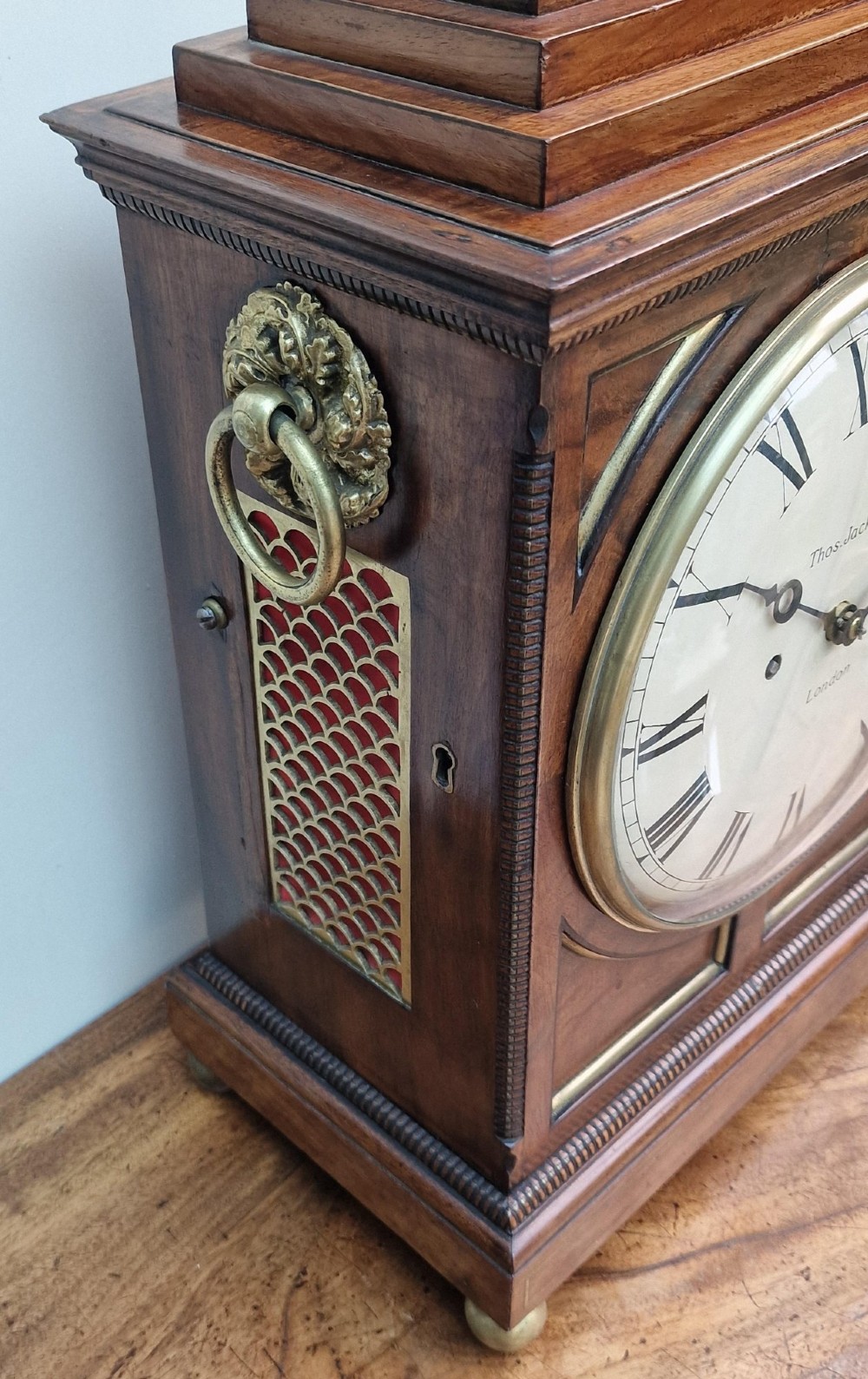 A Regency mahogany bracket clock featuring a white circular dial signed Thomas Jackson London, framed by brass stringing, lion head side handles, and a pineapple finial. View VII