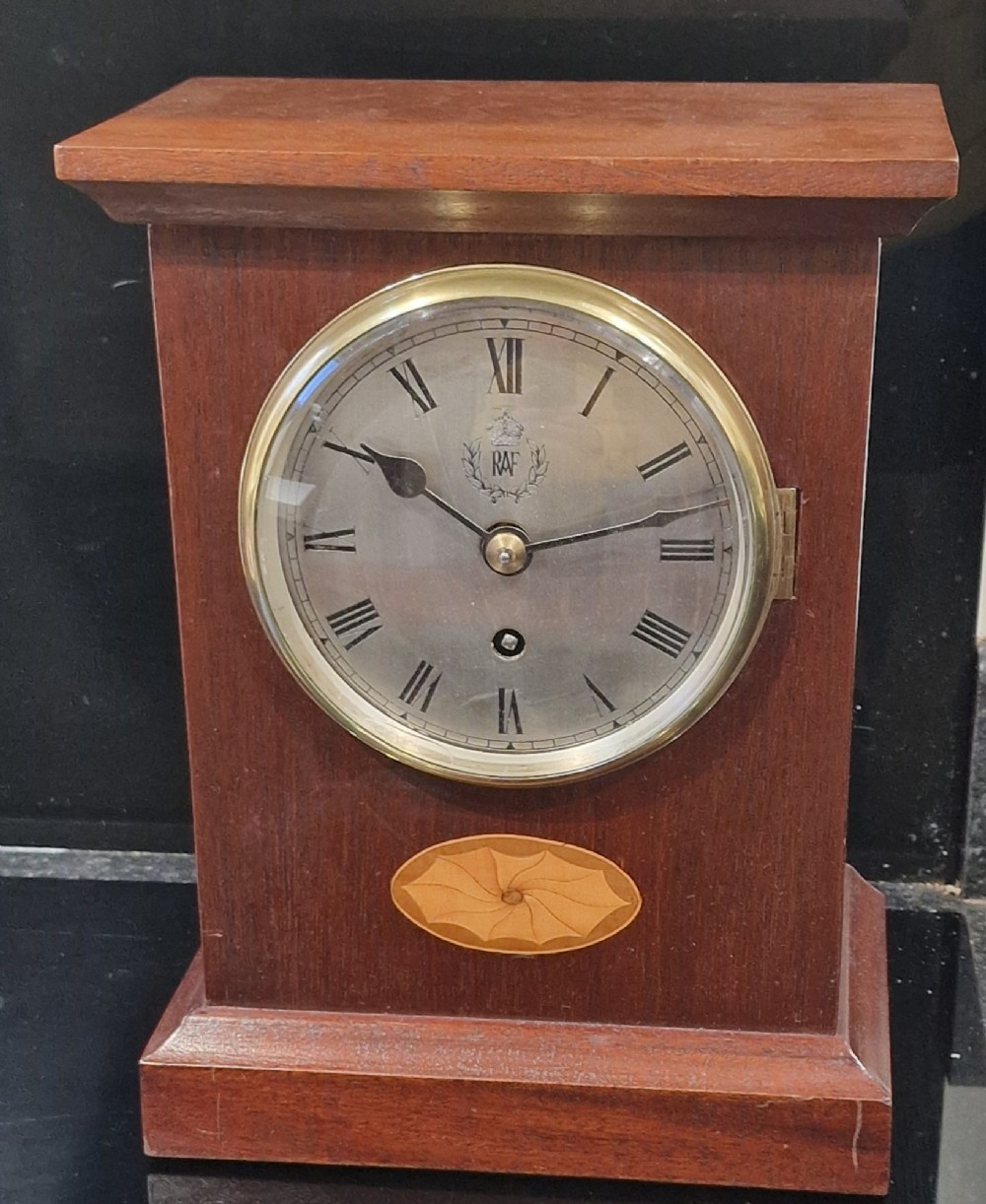 An upright wooden mantel clock featuring a brass-rimmed dial marked with the RAF crest and Roman numerals, set above an oval floral marquetry inlay on a stepped base.