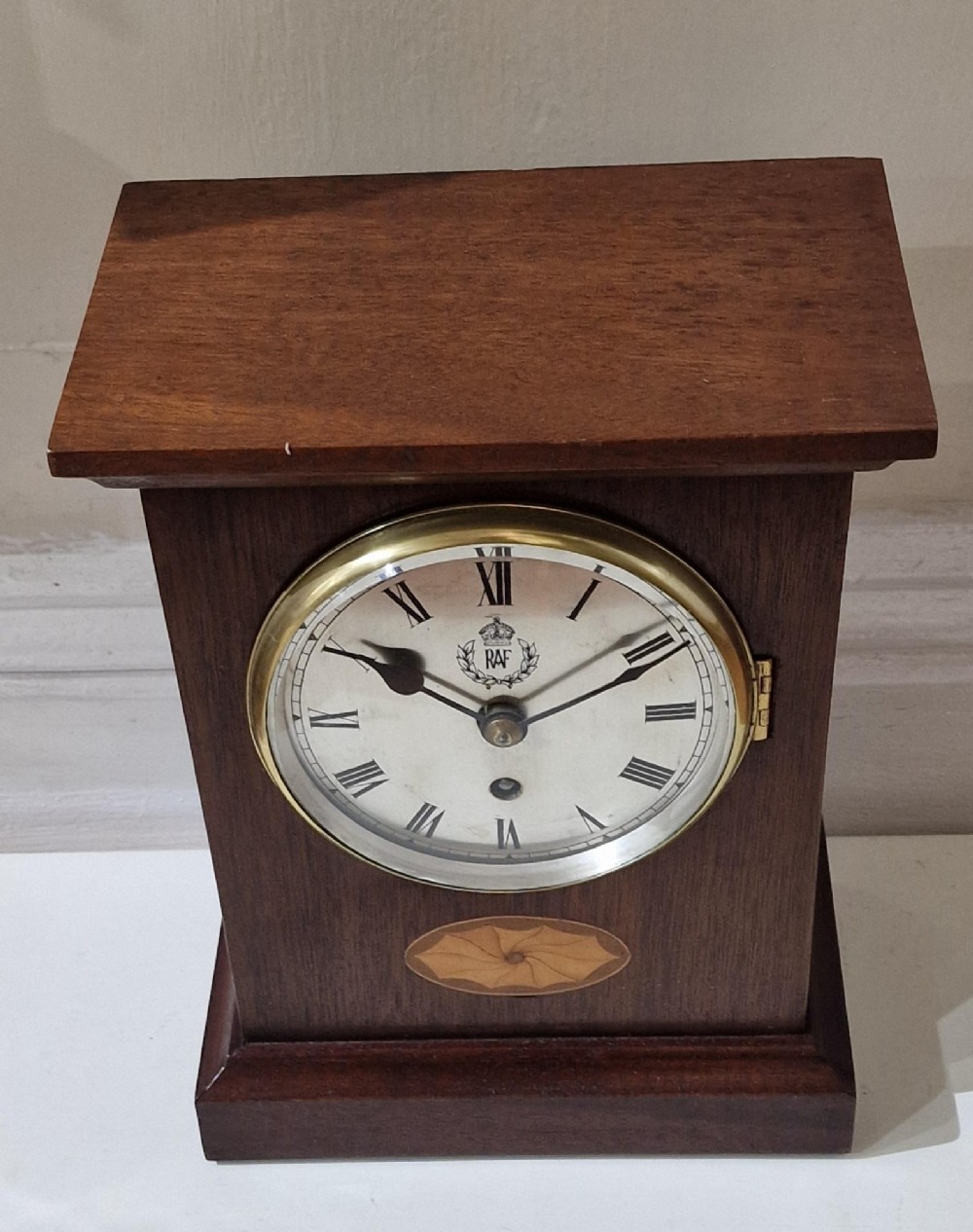 An upright wooden mantel clock featuring a brass-rimmed dial marked with the RAF crest and Roman numerals, set above an oval floral marquetry inlay on a stepped base. View VIII