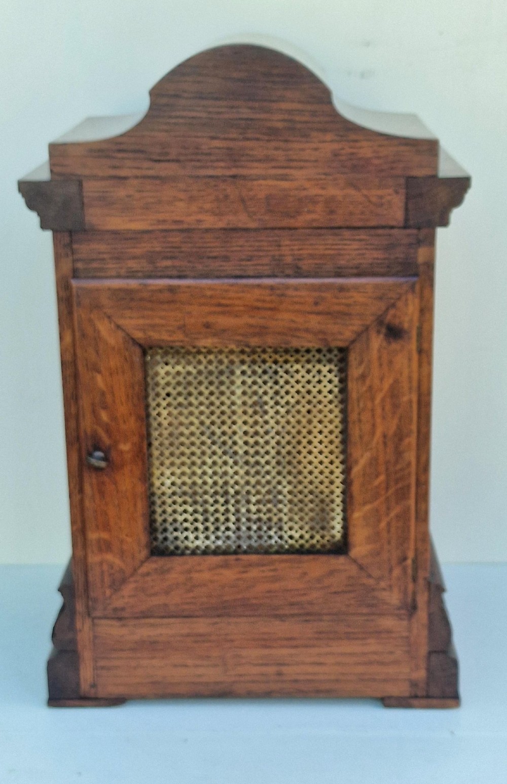 A carved oak mantel clock featuring an arched pediment, ornate brass dial with a silvered chapter ring, and a carved decorative base. View II
