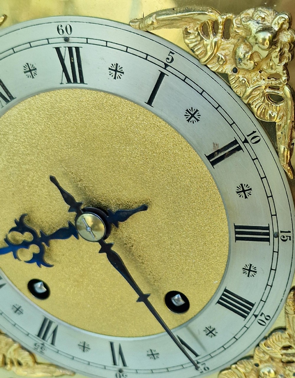 A carved oak mantel clock featuring an arched pediment, ornate brass dial with a silvered chapter ring, and a carved decorative base. View III