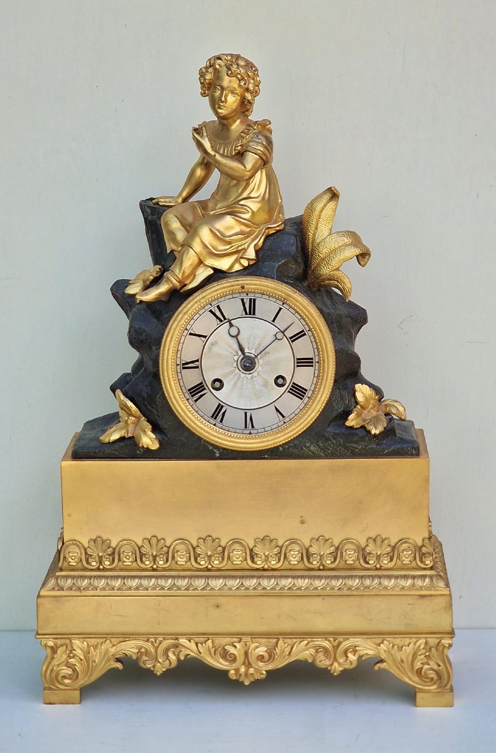 A 19th-century French gilt bronze and patinated bronze mantel clock featuring a seated gilded child figure atop a dark rock-form casing with Roman numerals.