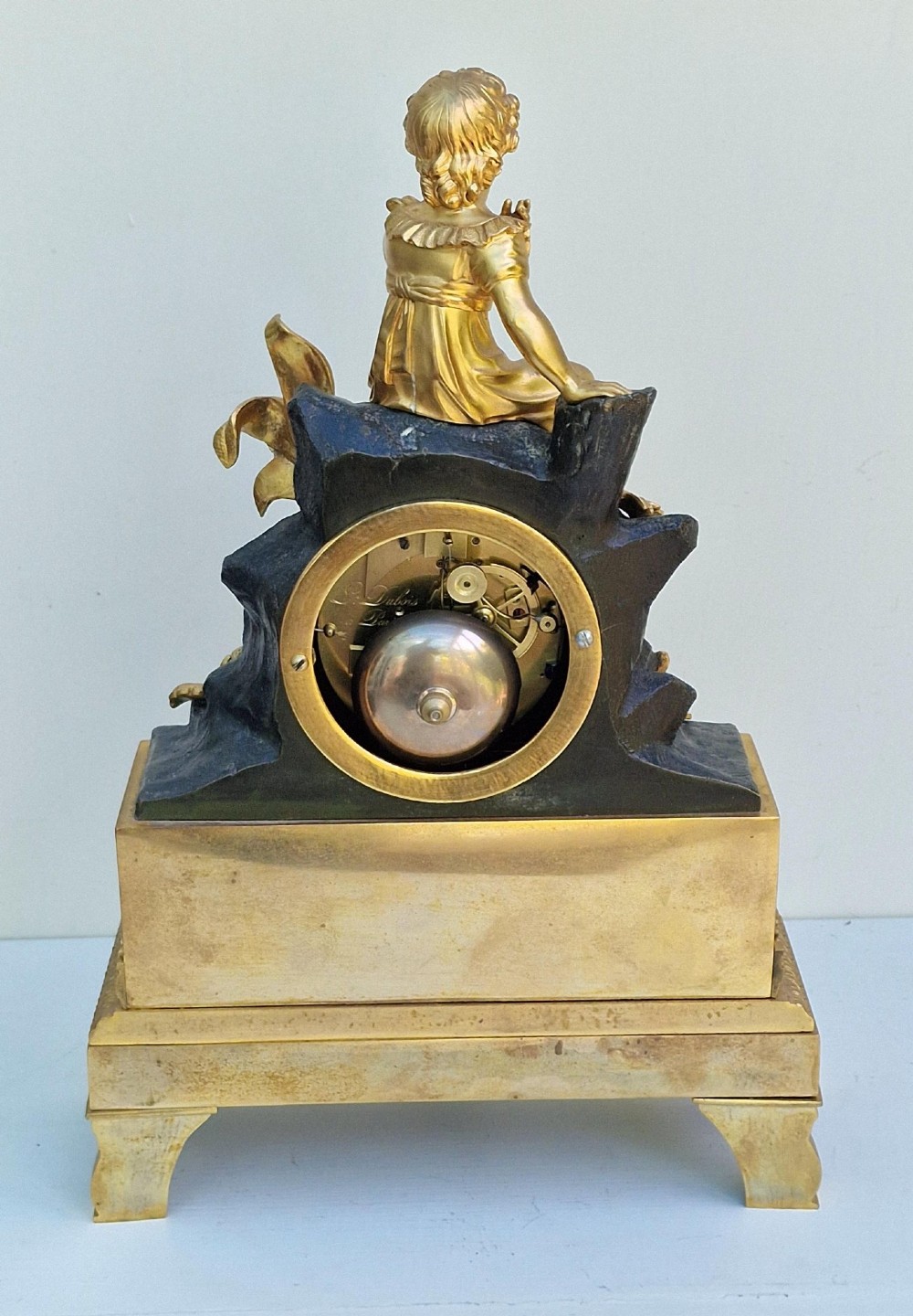 A 19th-century French gilt bronze and patinated bronze mantel clock featuring a seated gilded child figure atop a dark rock-form casing with Roman numerals. View II