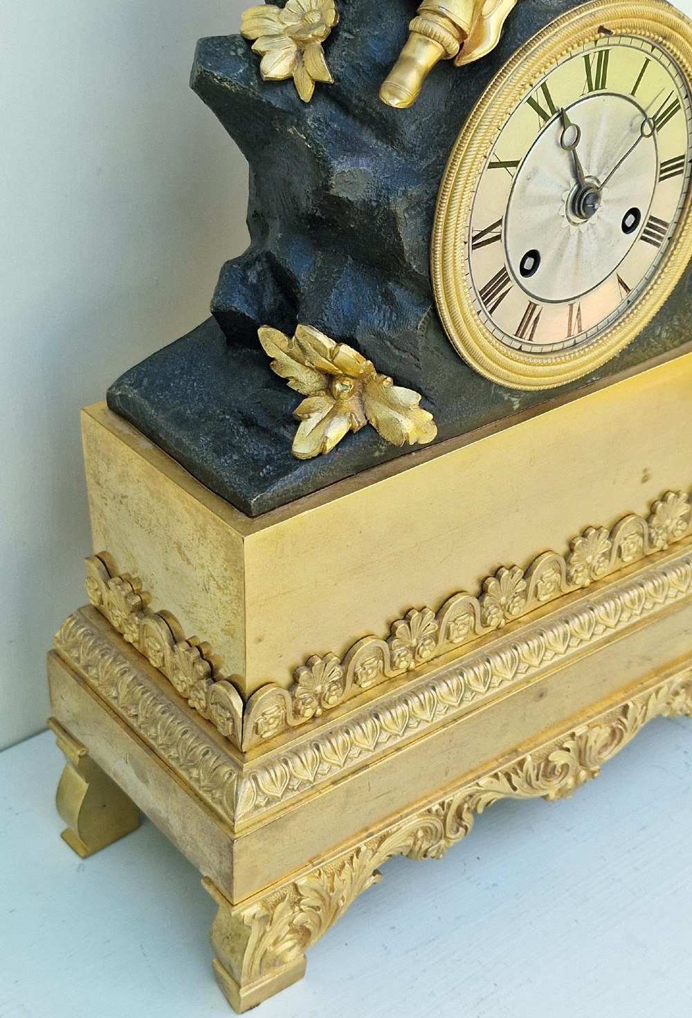 A 19th-century French gilt bronze and patinated bronze mantel clock featuring a seated gilded child figure atop a dark rock-form casing with Roman numerals. View IV
