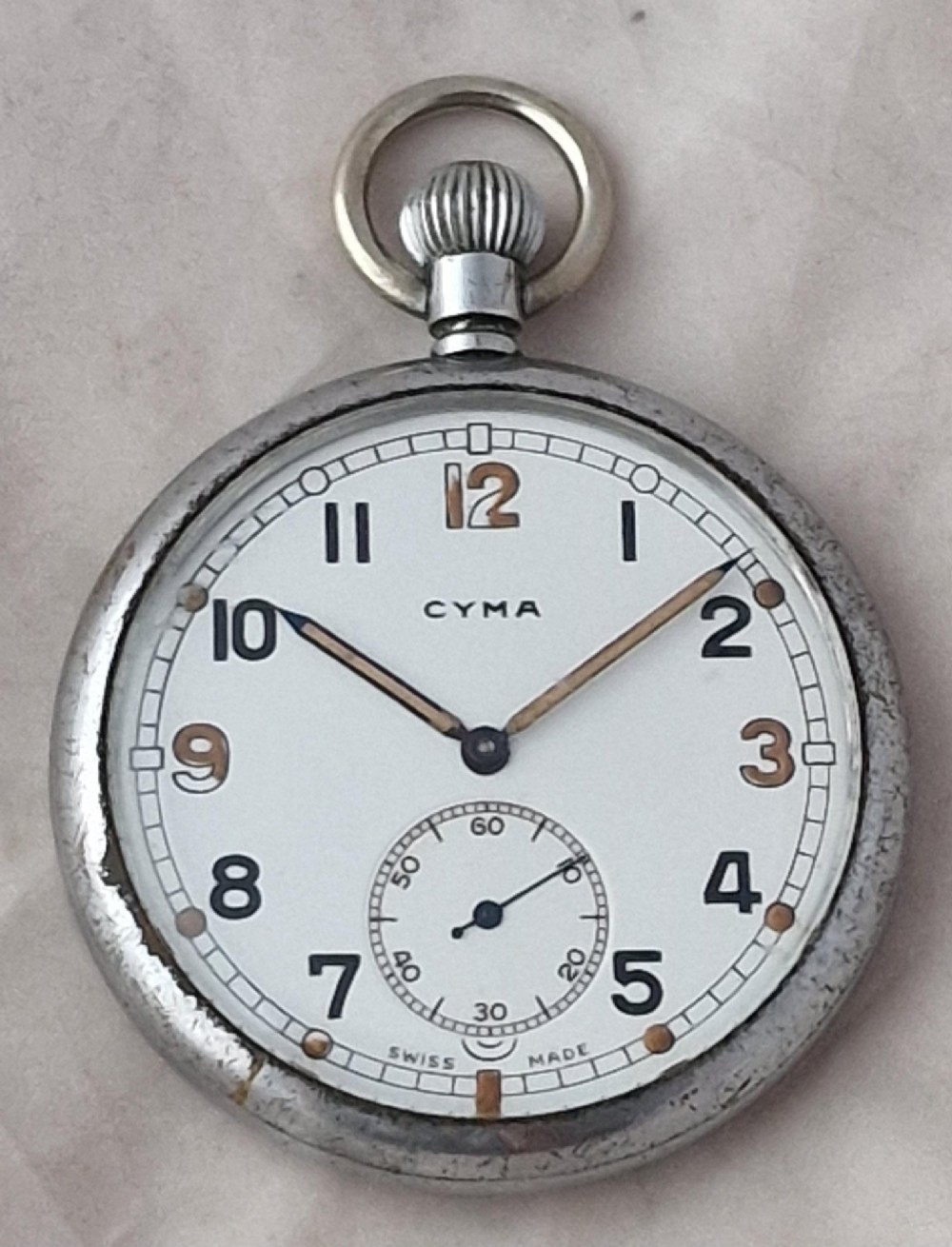 An open-face Cyma vintage pocket watch featuring a silver-coloured metal case, white dial, Arabic numerals, and a sub-seconds dial at six oclock.